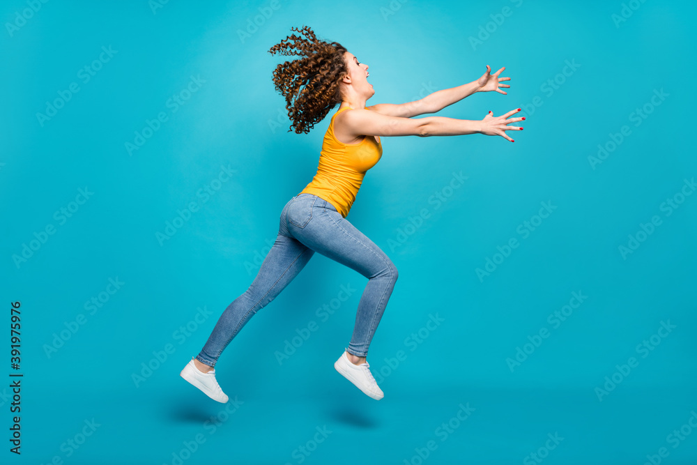 Funky wavy hairstyle lady jump high air spread arms wear casual yellow singlet jeans shoes isolated blue color background