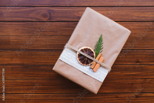 Wrapped gift box with natural decorations on brown rustic wooden background.