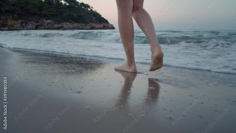 Camera follows woman walk barefoot on beautiful calm sandy beach at resort or hotel. Ocean waves surf roll over her feet. Concept tranquility and self care in peaceful setting