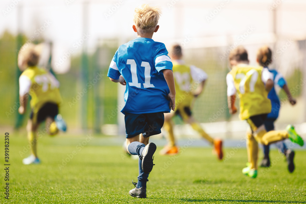 Obraz premium Boys playing in a soccer match. Football youth players kicking football ball in sunny day. Football competition tournament for school kids. Elementary age kids in blue and yellow sportswear