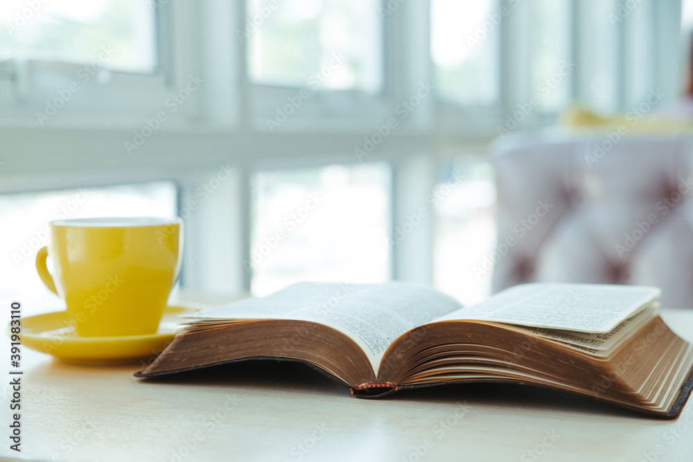 Open old book with yellow cup of coffee on the desk Open old book with yellow cup of coffee on the desk