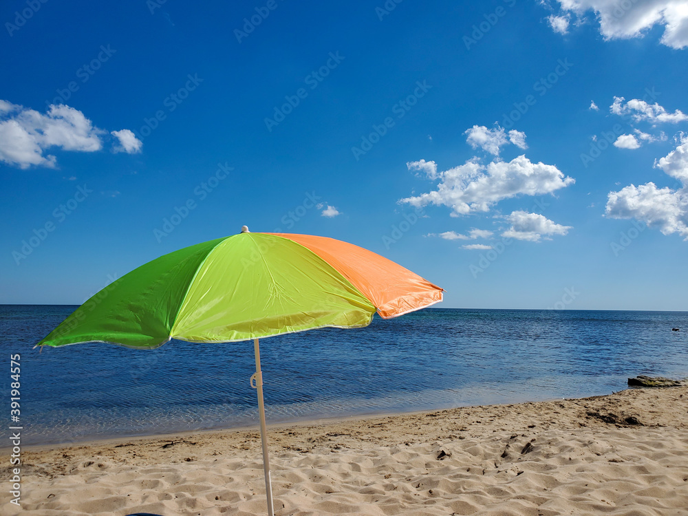 Yellow-orange sun umbrella on the beach of turquoise sea and blue sky.