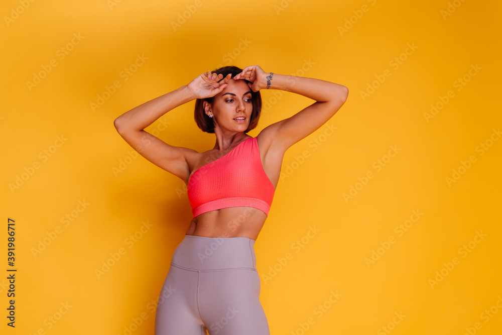 Sport and yoga lifestyle concept. Young fit pretty strong woman dressed in sport clothes, stylish top and leggings, poses against yellow background. Studio shot. Sport and yoga lifestyle concept. Young fit pretty strong woman dressed in sport clothes, stylish top and leggings, poses against yellow background. Studio shot.