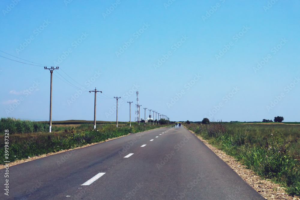 Fototapeta premium Una solitaria carretera rural en la Rumanía. Carretera de doble sentido entre campos de cultivo en un soleado día de verano.