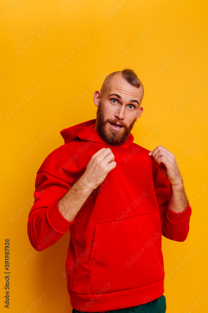 Happy caucasian handsome brutal bearder man wearing warm red winter trendy fleece hoodie, studio shot, yellow background. Happy caucasian handsome brutal bearder man wearing warm red winter trendy fleece hoodie, studio shot, yellow background.