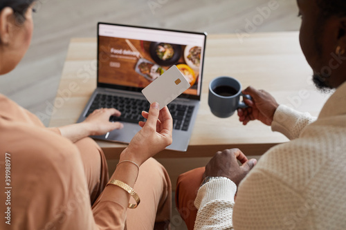 Rear view of couple sitting in front of the laptop and using credit card for online shopping