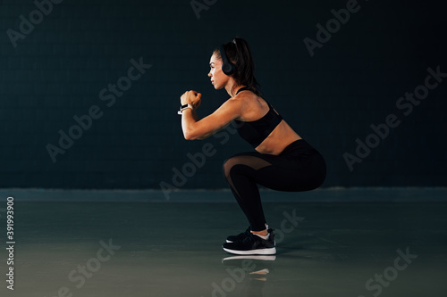 Side view of muscular woman with headphones doing squats in gym