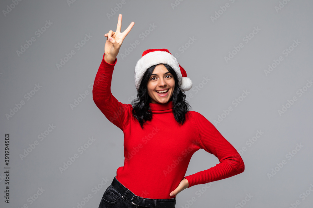 Joyful young Santa woman with Christmas hat showing victory sign isolated on grey wall background Joyful young Santa woman with Christmas hat showing victory sign isolated on grey wall background