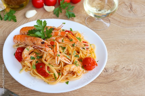  Italian Traditional Dish"Linguine agli Scampi" or "Linguine with Scampi Shirmps",linguine with scampi,cherry tomatoes,white wine,olive oil,parsley,garlics and peppers on white plate with wooden table
