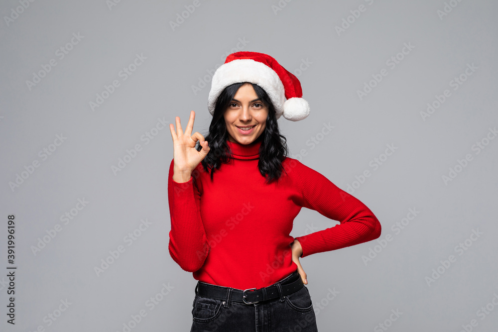 Woman with christmas hat over isolated blue background showing an ok sign with fingers Woman with christmas hat over isolated blue background showing an ok sign with fingers