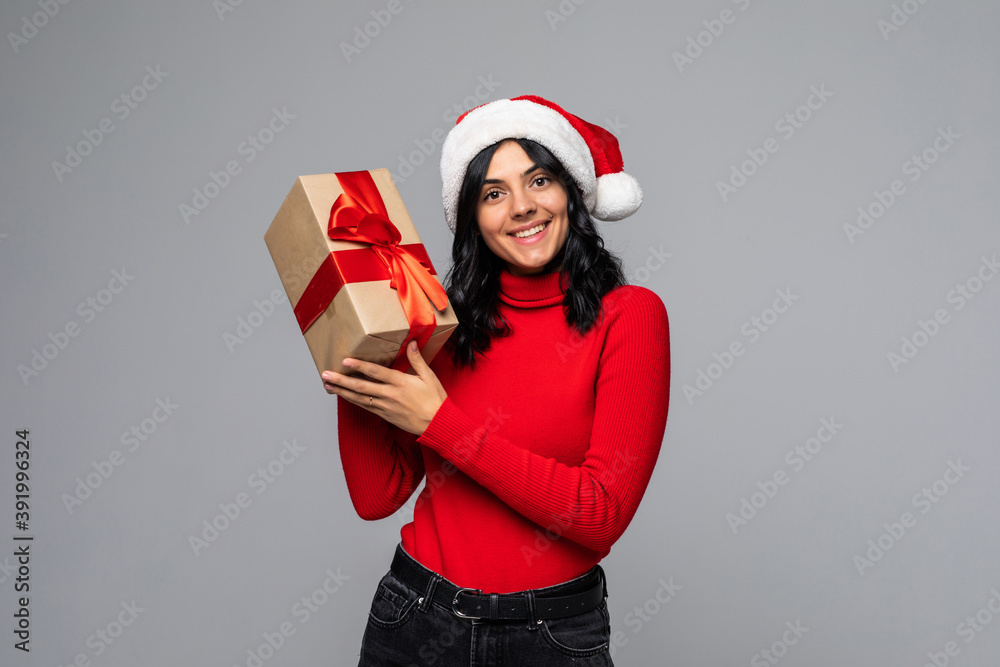 Happy excited young woman in santa claus hat with gift box isolated over gray background Happy excited young woman in santa claus hat with gift box isolated over gray background