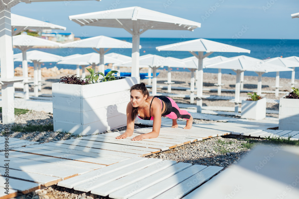 Beautiful brunette woman sports yoga on the beach by the sea in the morning