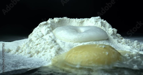 A mixture of flour and baking soda rising. Raw chicken egg near mound of flour. Cooking in front of a black background.Close up shot. Zoom in. photo