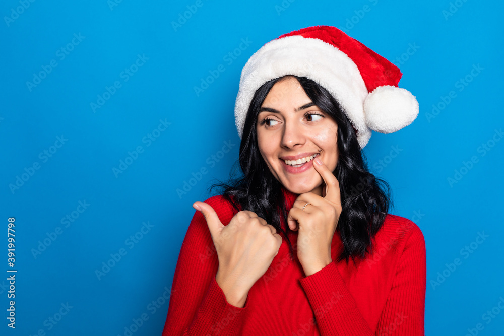 Woman with christmas hat pointing to the side to present a product isolated on blue background Woman with christmas hat pointing to the side to present a product isolated on blue background