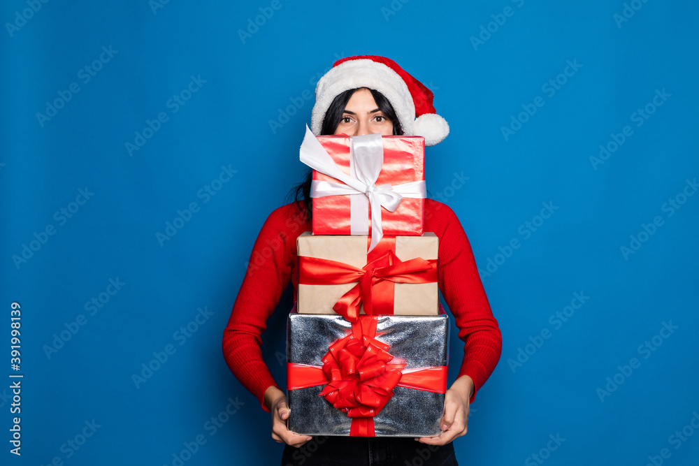 Young woman in Santa hat showing Christmas gift on blue background