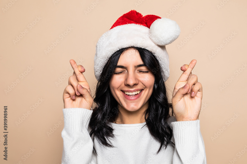 Yuong woman with fingers crossing weat christmas hat over isolated beige background Yuong woman with fingers crossing weat christmas hat over isolated beige background