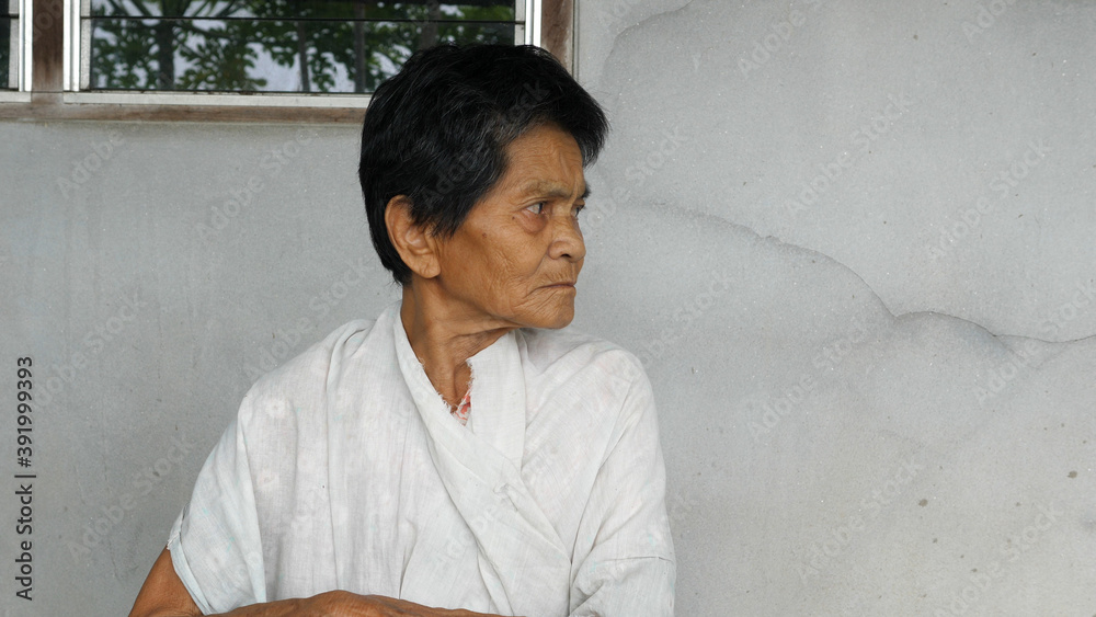 Obraz premium Asian old woman looking side way with relax face isolated concrete grey wall background. Rural lifestyle concept.