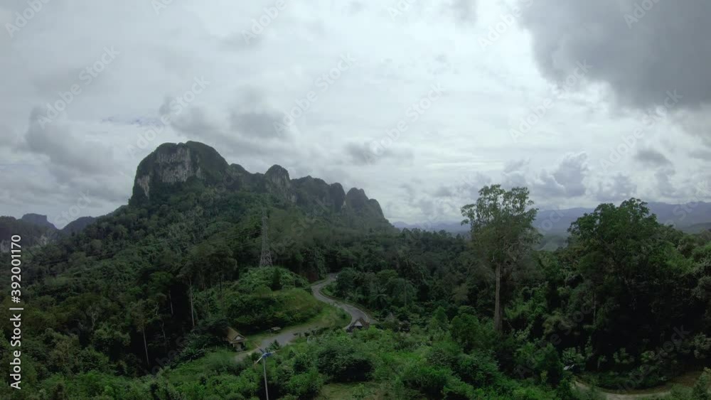 Huge lush mountain in tropical country, electricity tower and curvy road in cloudy day. dark clouds moving b-roll over the mount with sun shining on the tree. nature tourism background. Huge lush mountain in tropical country, electricity tower and curvy road in cloudy day. dark clouds moving b-roll over the mount with sun shining on the tree. nature tourism background.