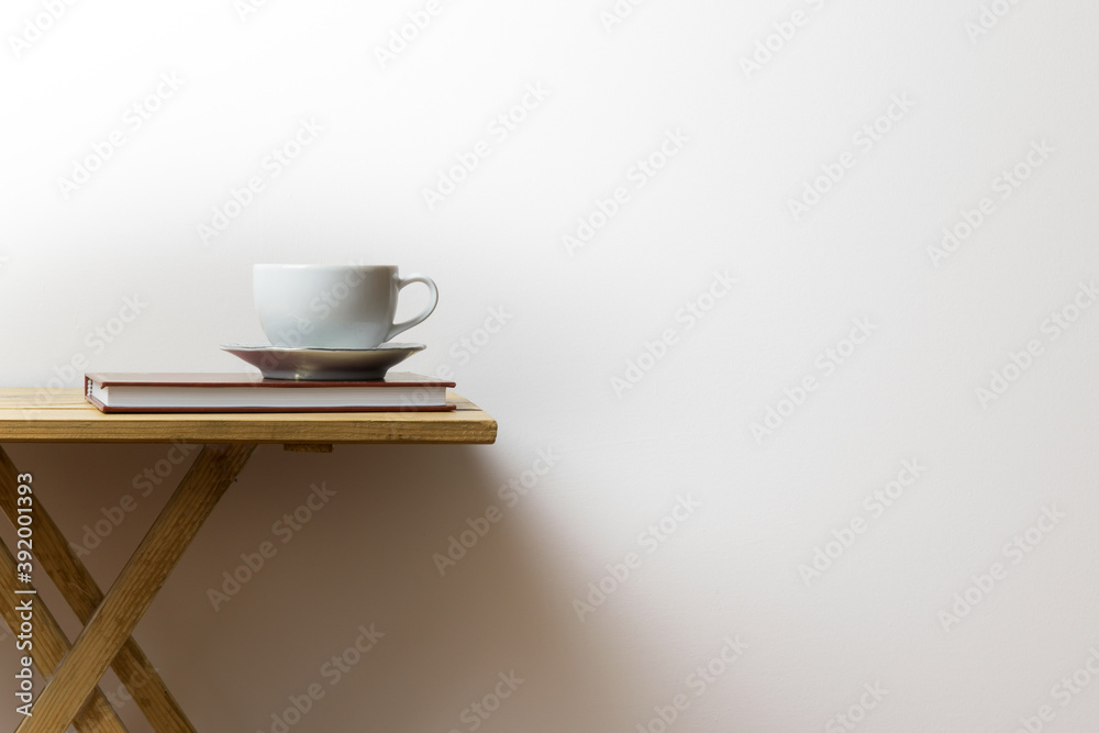 White cup of coffee on a book and on a wooden table, white background
