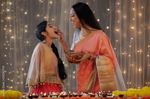 Young girl eating sweets through her mother's hand	 photo