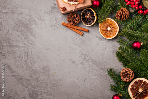 Christmas composition. Gift box, balls, cinnamon, anise, dried fruits, pine cones and fir needles decorations on grey background. Top view copy space