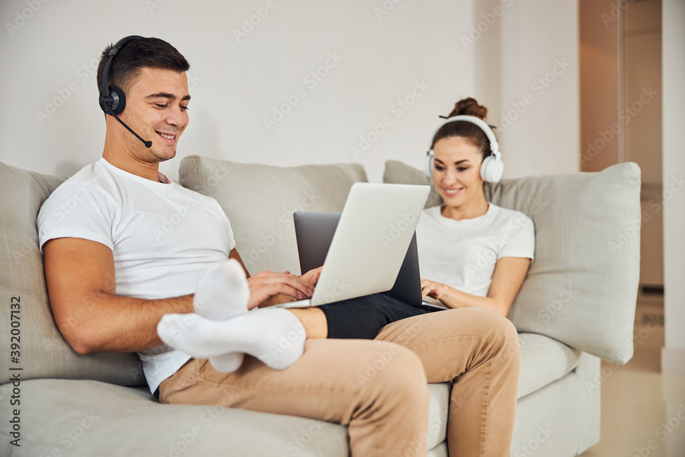 Brunette man and lovely lady sitting on couch with laptops