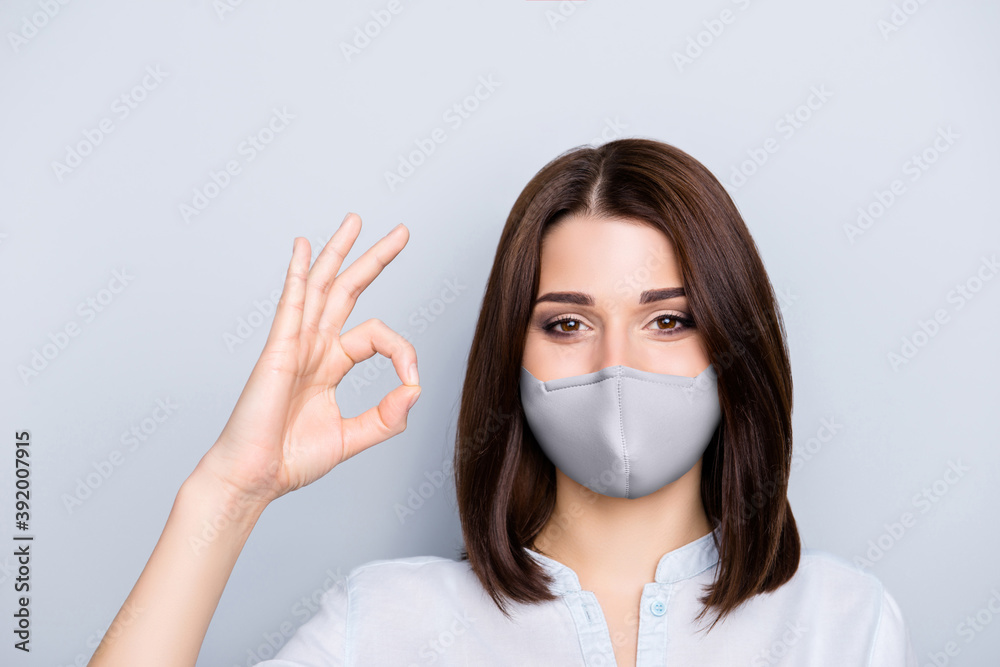 Photo portrait of girl showing ok-sign wearing grey fabric face mask isolated on grey colored background Photo portrait of girl showing ok-sign wearing grey fabric face mask isolated on grey colored background