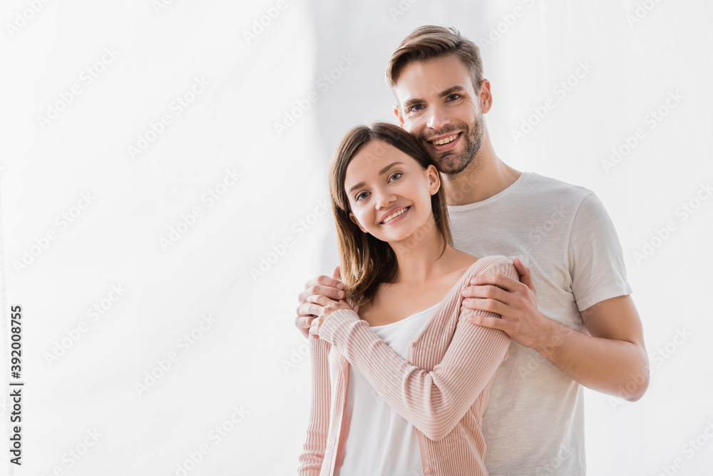 happy man embracing cheerful wife and looking at camera happy man embracing cheerful wife and looking at camera