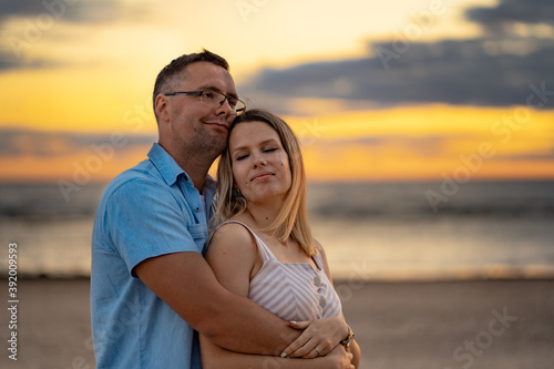 a portrait of happy couple. A man in glasses hugging his young wife. Beautiful sea and sunset on background.Honeymoon concept © Yulia Raneva