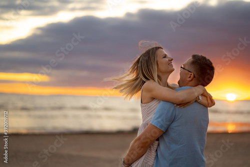 a portrait of happy couple. A man in glasses and young blond woman enjoying summer evening on the beach. Beautiful sea and sunset on background. Honeymoon concept