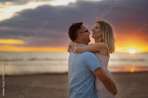 a portrait of happy couple. A man in glasses and young blond woman enjoying summer evening on the beach. Beautiful sea and sunset on background. Honeymoon concept
