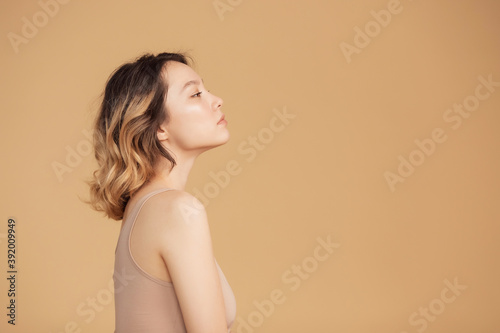 Profile young girl of Asian appearance with wavy streaked hair on beige background. Concept beauty and fashion of face and body skin