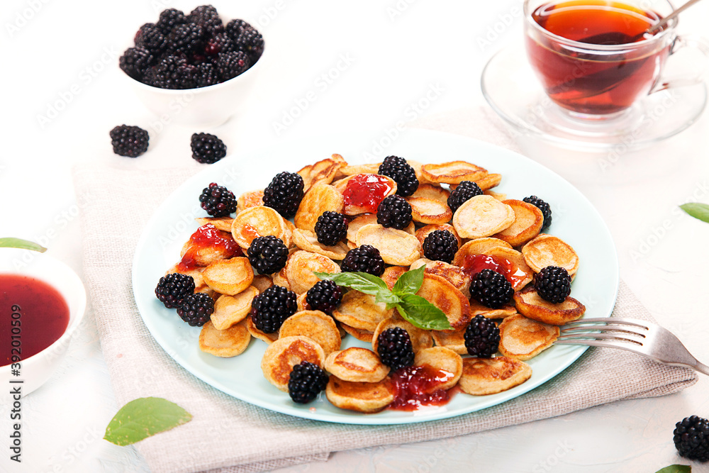 Mini-pancake dessert with blackberries, decorated with mint leaves, jam and tea in a glass bowl, two forks on a white plate. Healthy breakfast. Mini-pancake dessert with blackberries, decorated with mint leaves, jam and tea in a glass bowl, two forks on a white plate. Healthy breakfast.
