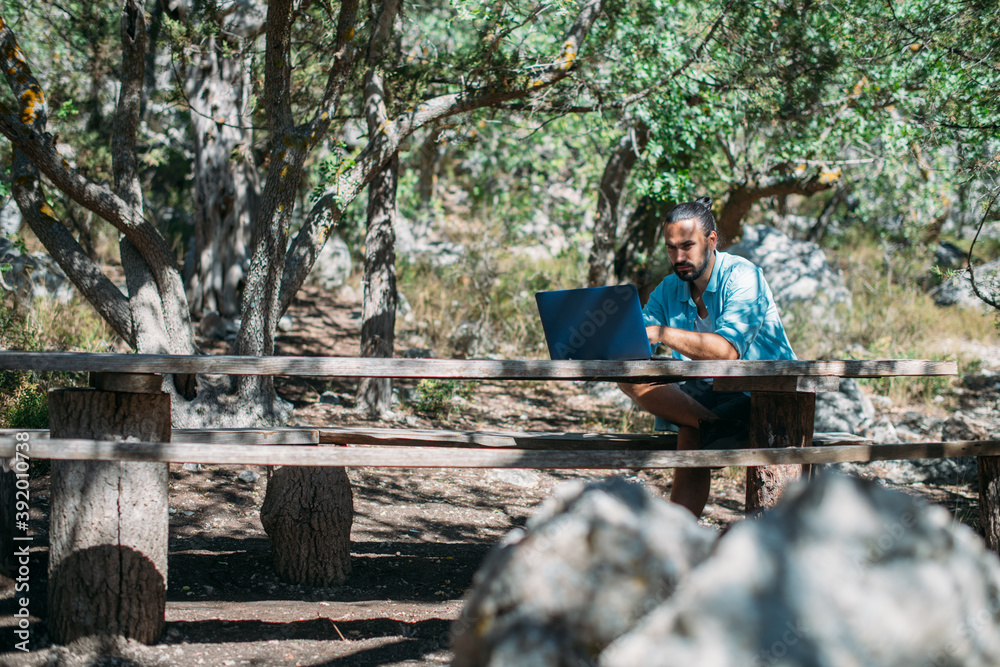 Fototapeta premium Male tourist working on a laptop outdoors in a camping.