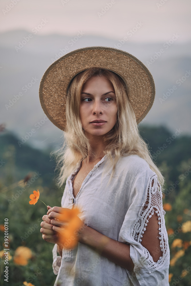 The blonde in a linen dress walks among herbs and wildflowers on a meadow in the mountains. A woman in the Boho style, resting in the countryside, a simple village lifestyle