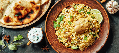 Pakistani food - biryani rice with chicken and raita yoghurt dip. Delicious hyberabadi chicken biryani on dark background. Top view or flat lay. Copy space for text or design. Long horizontal banner