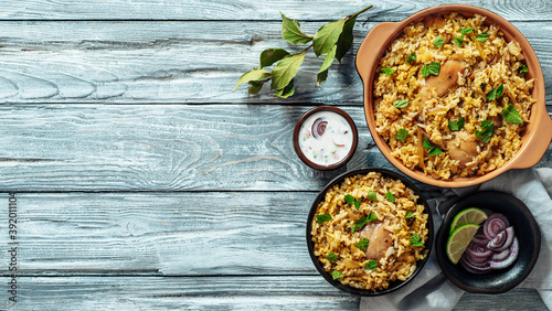 Pakistani food - biryani rice with chicken and raita yoghurt dip. Delicious hyberabadi chicken biryani on gray wooden background. Top view or flat lay. Copy space for text or design. Banner