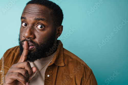 Surprised african american man showing silence gesture at camera