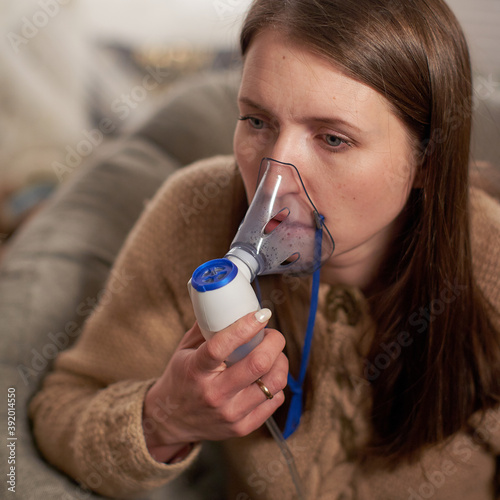 woman makes inhalation nebulizer at home. holding a mask inhaling fumes spray the medication into your lungs sick patient. self-treatment of the respiratory tract using inhalation nebulizer photo