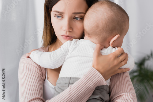фотографія worried mother holding in arms baby boy and looking away