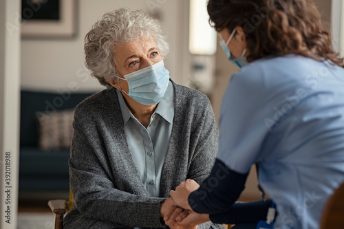 Female doctor consoling senior woman wearing face mask during home visit