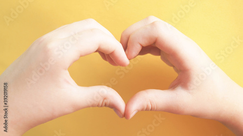 Child making heart shape hands on yellow background. Concept of  Heart Health  Hopeful  Love  Business  Idea  Donate  Charity  Kindness  Pleasure