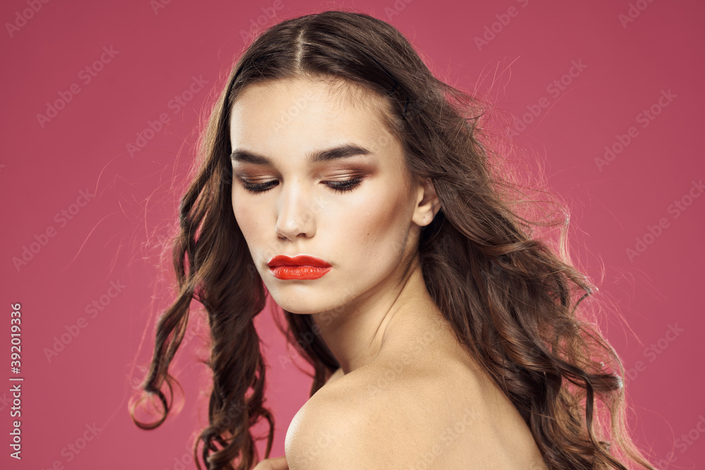 Beautiful brunette woman with makeup on her face on a pink background naked shoulders