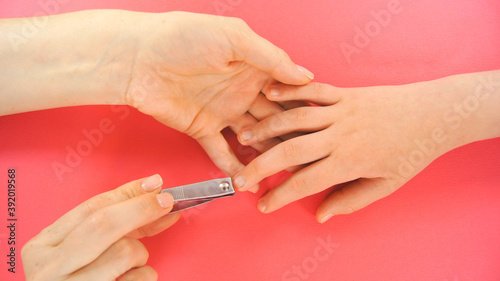 Hands cuts child s nails. Close up and pink background