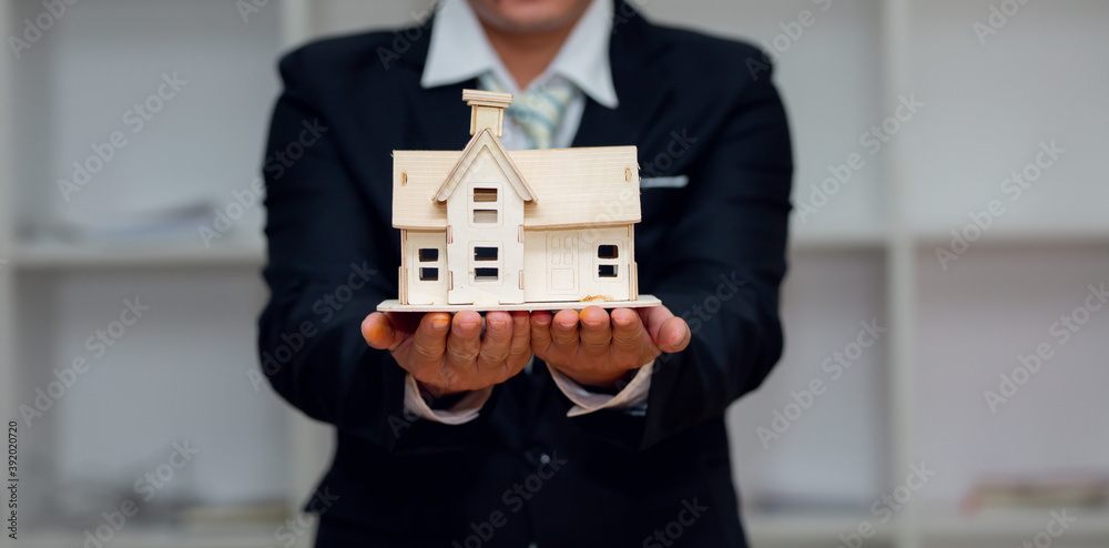 Investment in Housing Concept. Business man hand hold a home model as an investment in real estate