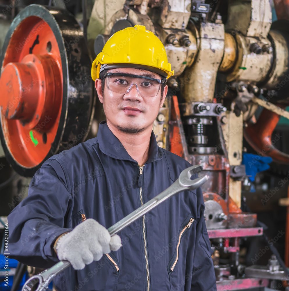 A worker in uniform and hard hat showing a wrench. A worker in uniform and hard hat showing a wrench.