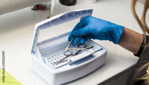 Woman in blue gloves sterilizes manicure tools in the nail tool sterilizer machine. Safe concept. Safe manicure and pedicure. Image for beauty salon and sites about manicure. Beauty sphere.