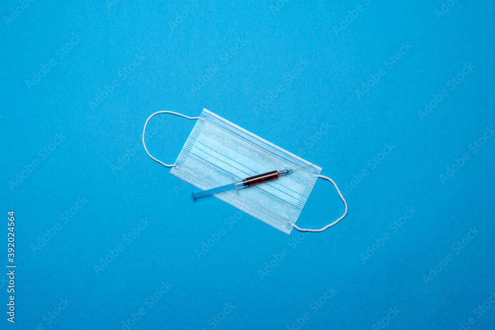 Syringe and disposable face mask to prevent COVID-19 virus on blue background Syringe and disposable face mask to prevent COVID-19 virus on blue background