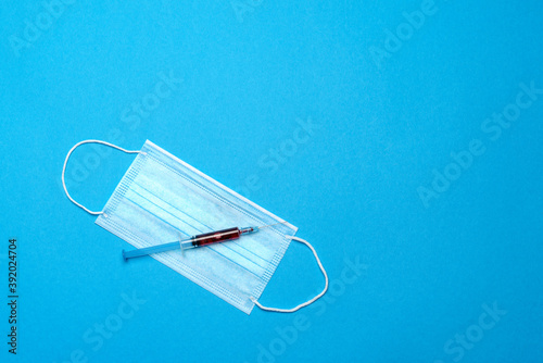 Syringe and disposable face mask to prevent COVID-19 virus on blue background