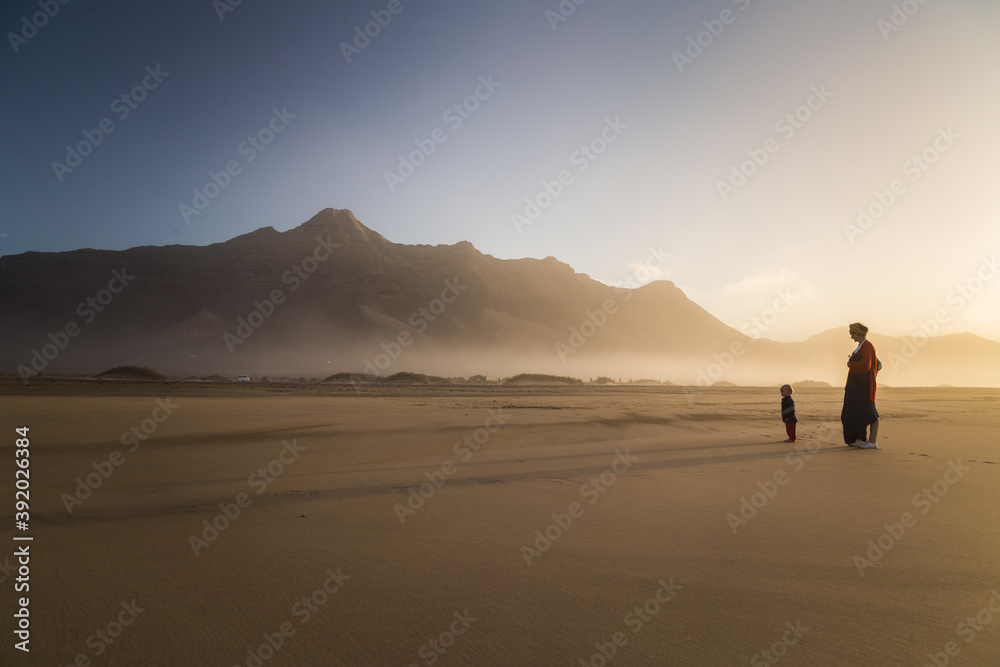 Silhouette of young mother with her little child walking on sunshine in Cofete, Fuerteventura, Canary Islands, Spain. Silhouette of young mother with her little child walking on sunshine in Cofete, Fuerteventura, Canary Islands, Spain.